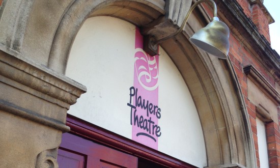 Close up of the tall arched wooden door with a ref and black theatre sign saying Thame Players Theatre over the lintel.