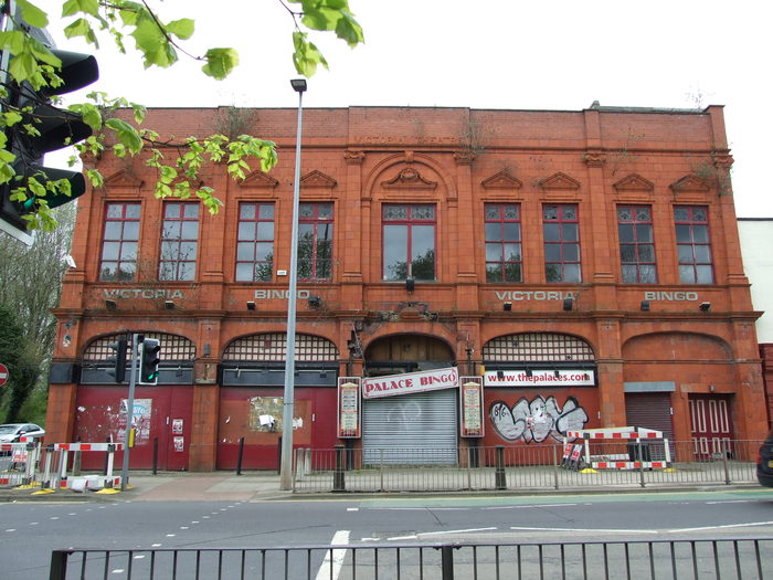 Streetscape showing the full facade of the red brick Salford Victoria Theatre from across the street.