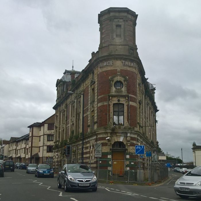 Swansea Palace Theatre from the road with railings around the ground floor, and shrubbery growing from the facade.