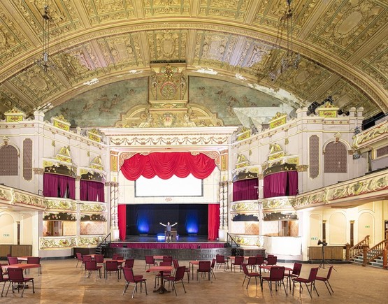 Auditorium of Morecambe Winter Gardens set up with circular tables with chairs around them. 