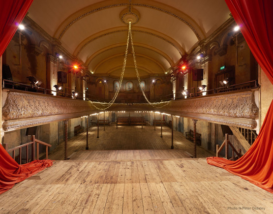 Auditorium of Wilton's Music Hall with wooden floors and red curtain