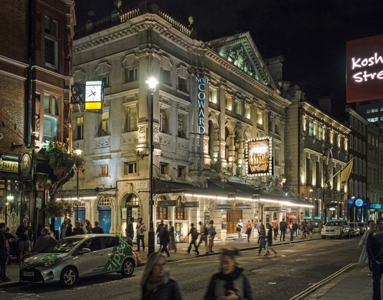 Busy street in front of the Noel Coward theatre in London's West End at night.