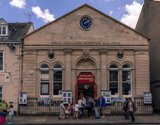 Exterior of Wallingford Corn Exchange, a stone building, with a crowd of people in the street outside