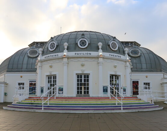 The entrance to Worthing Pavilion Theatre, gleaming in the morning sun, with rainbow=coloured steps ascending to its front door.