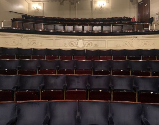Blue fabric and dark brown wood framed seats in the auditorium of Ambassadors Theatre.