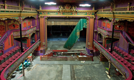 Interior and stage of derelict theatre with ornate and colourful plasterwork, viewed from the balcony