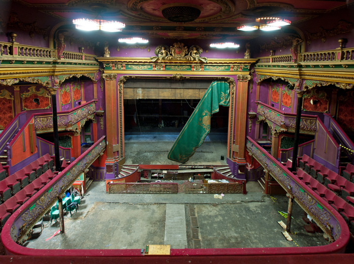 Interior and stage of derelict theatre with ornate and colourful plasterwork, viewed from the balcony
