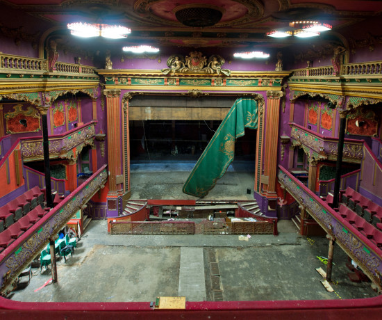 Interior and stage of derelict theatre with ornate and colourful plasterwork, viewed from the balcony