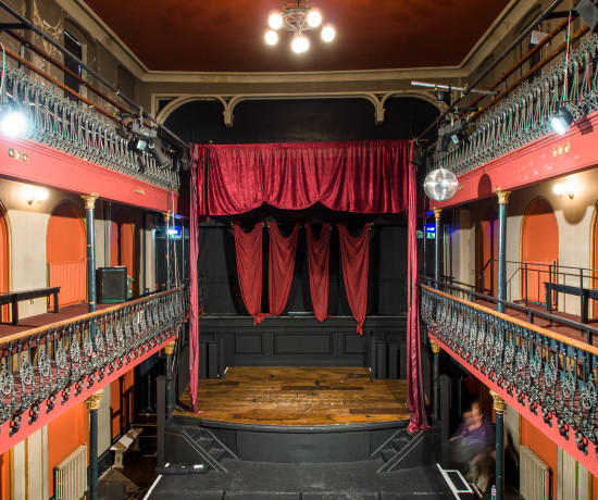 Auditorium of Hoxton Hall, historic music hall viewed from the balcony showing stage and red curtain