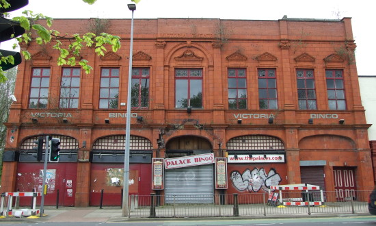 Streetscape showing the full facade of the red brick Salford Victoria Theatre from across the street.