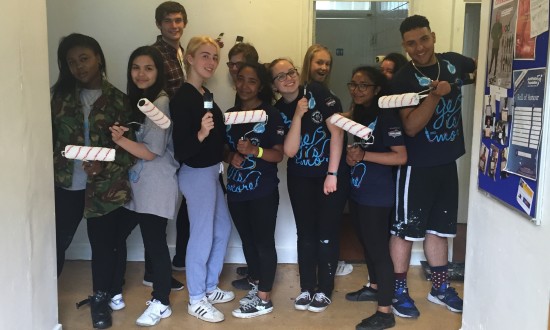 Youth volunteer decorators holding paintbrushes posing in the doorway.