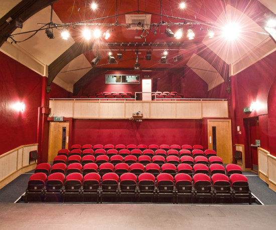 Rows of red auditorium seats in a small community theatre viewed from the stage.