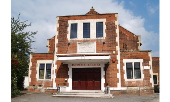 The exterior of Intimate Theatre, with a car parking area in the foreground.