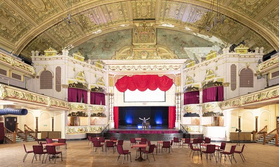 Auditorium of Morecambe Winter Gardens set up with circular tables with chairs around them. 