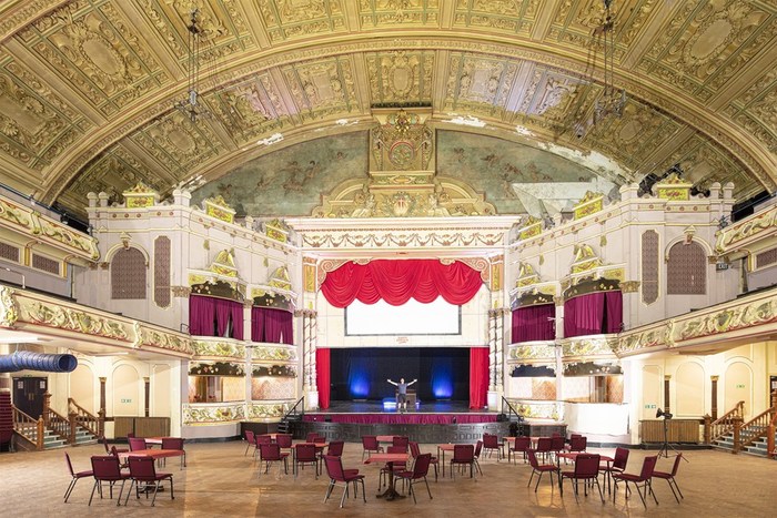 Auditorium of Morecambe Winter Gardens set up with circular tables with chairs around them. 