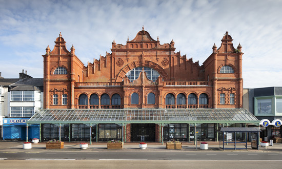 The red brick and terracotta exterior of Morecambe Winter Gardens, with a symmetrical composition with a big central gable flanked by projecting square towers with shaped gables