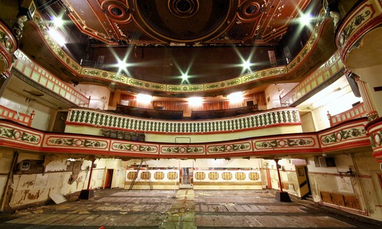 The auditorium of Salford Victoria, with its 3 balconies but no seats. Balcony fronts are either swagged or balustraded in beige,and gold with red accents