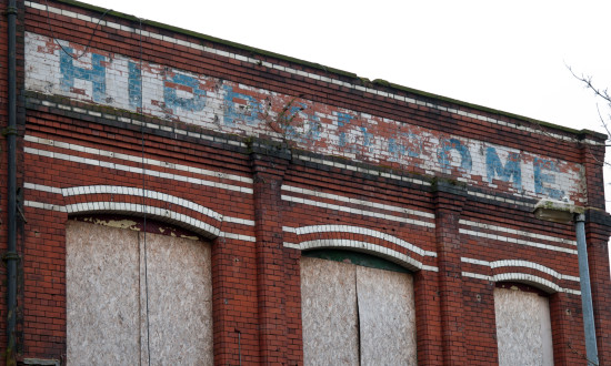 A section of the red brick façade with a  painted sign with blue HIPPODROME written on a white painted background