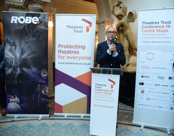 Tim Eyles speaking at Conference 19 reception, positioned between two branded banners