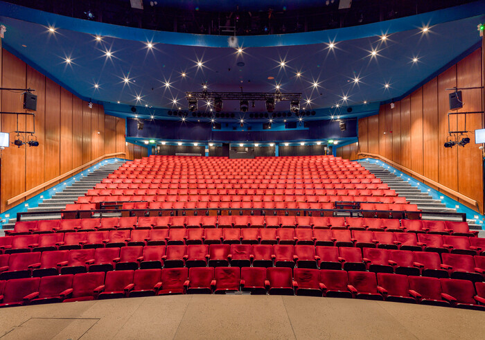 Auditorium of Queen's Theatre Hornchurch, viewed from the stage, showing rows of red seats, wood panelled walls and dark blue ceiling with twinkling lights