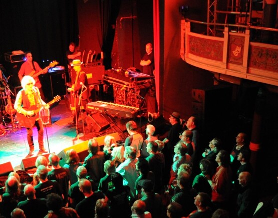 Band performing on stage in front of a full audience, viewed from the balcony