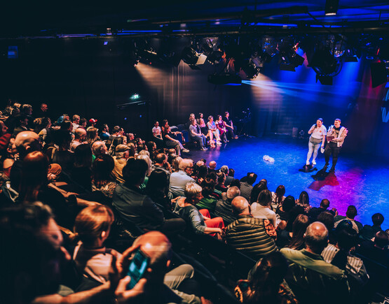 Busy audience watching two performers on stage at Unity Theatre